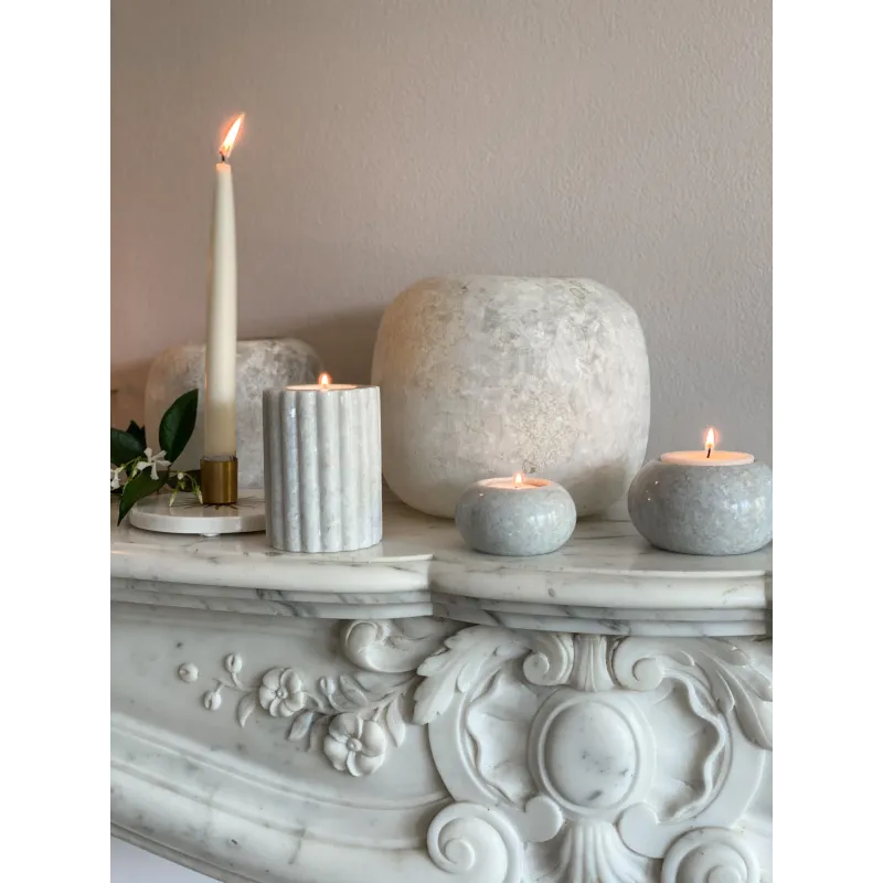 Le bougeoir en marbre blanc M placé sur une cheminée, entouré d’autres éléments décoratifs.