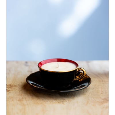 Bougie parfumée dans une élégante tasse à café noire avec intérieur rouge et bordure dorée.