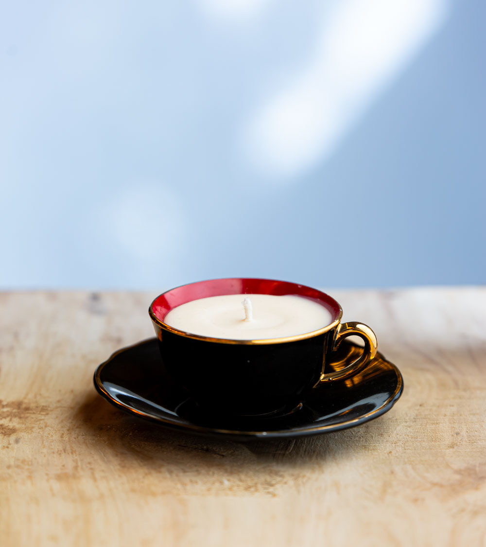 Bougie parfumée dans une élégante tasse à café noire avec intérieur rouge et bordure dorée.