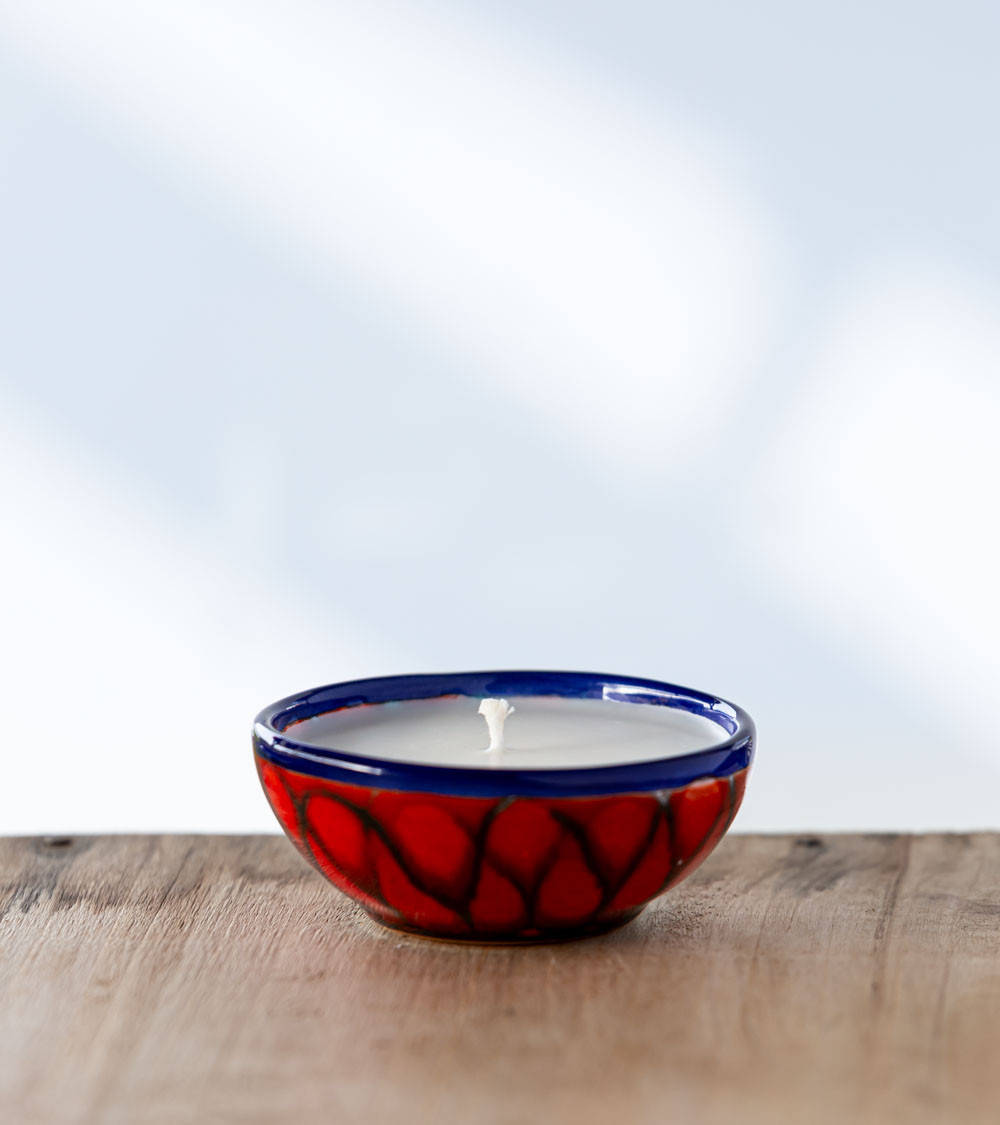 Bougie parfumée dans une coupe rouge et bleu aux motifs élégants.